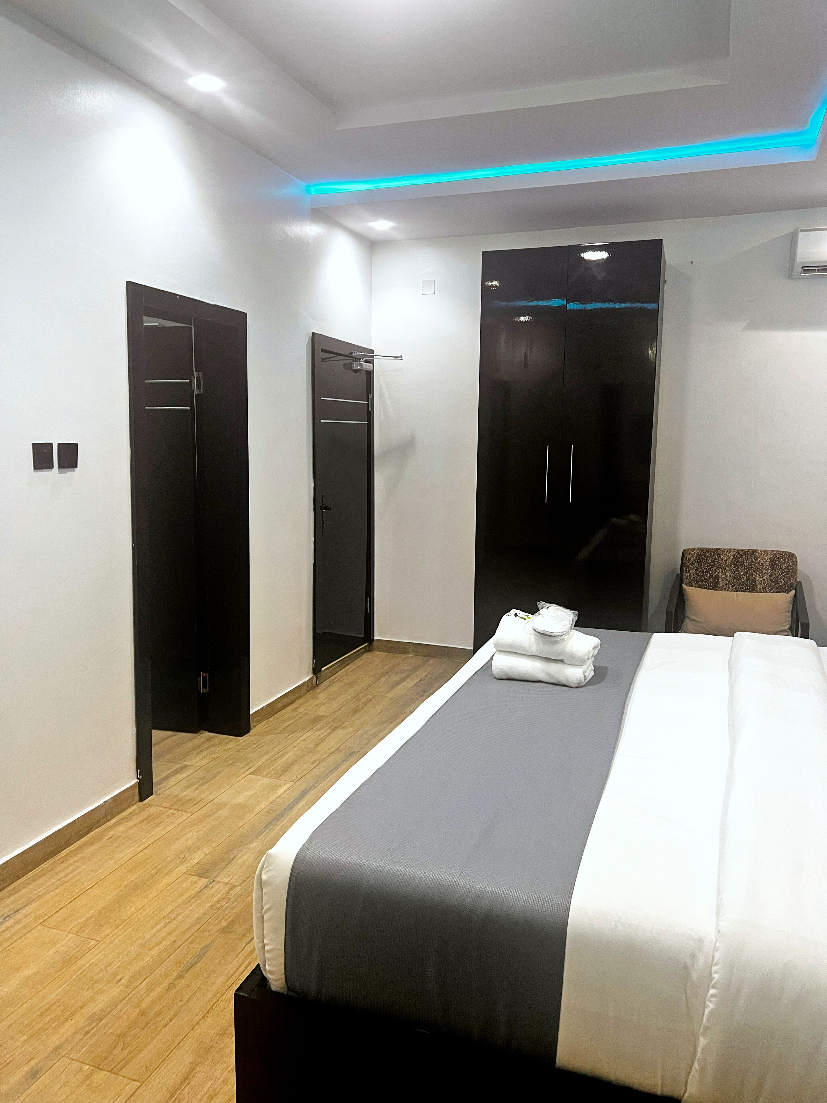 Ein modernes Hotelzimmer mit einem aufgeräumten Bett, einer Sitzecke mit einem Sessel und einem Kleiderschrank.