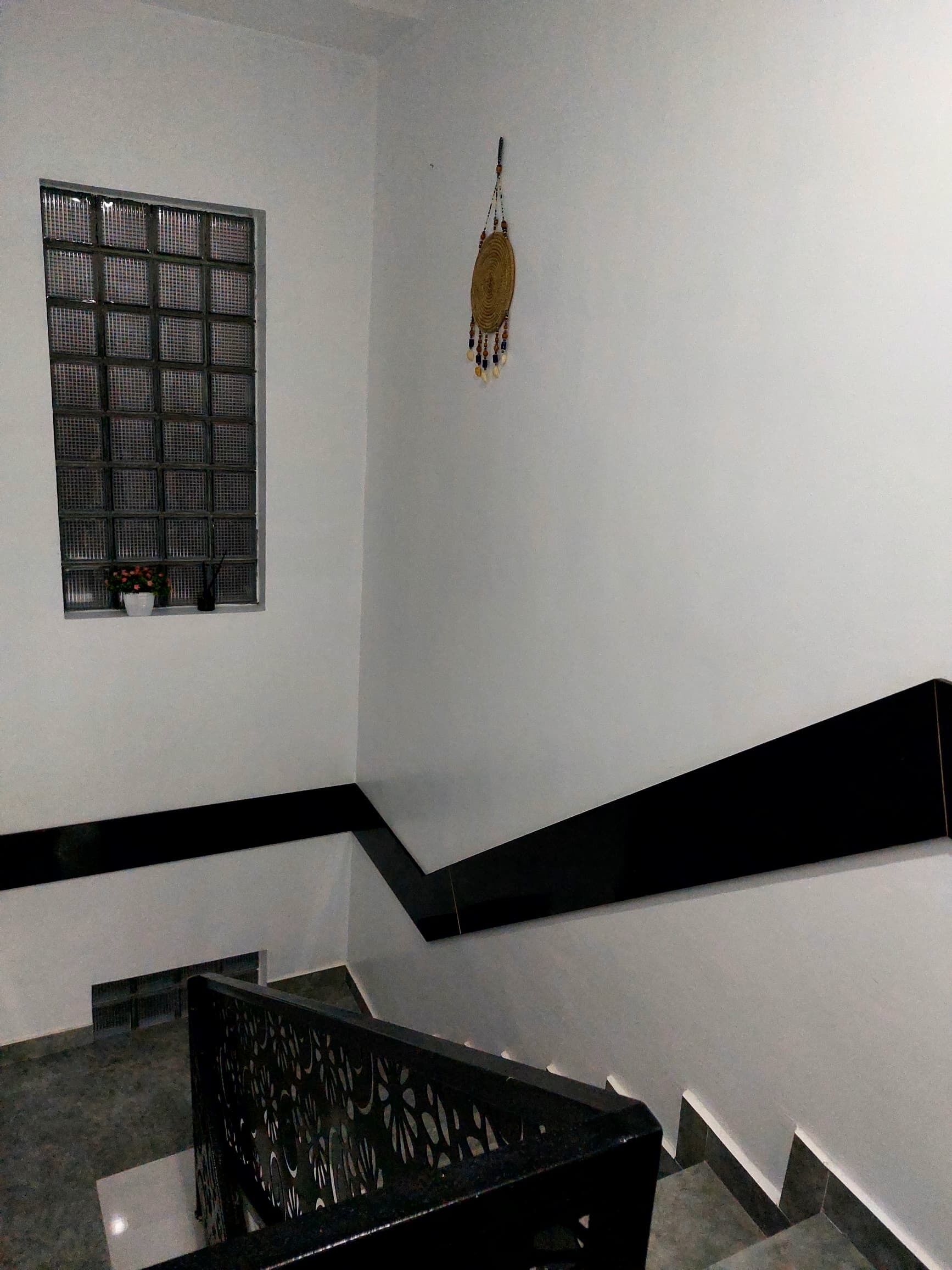 A staircase with a black handrail and a white wall with a window and a hanging decoration.
