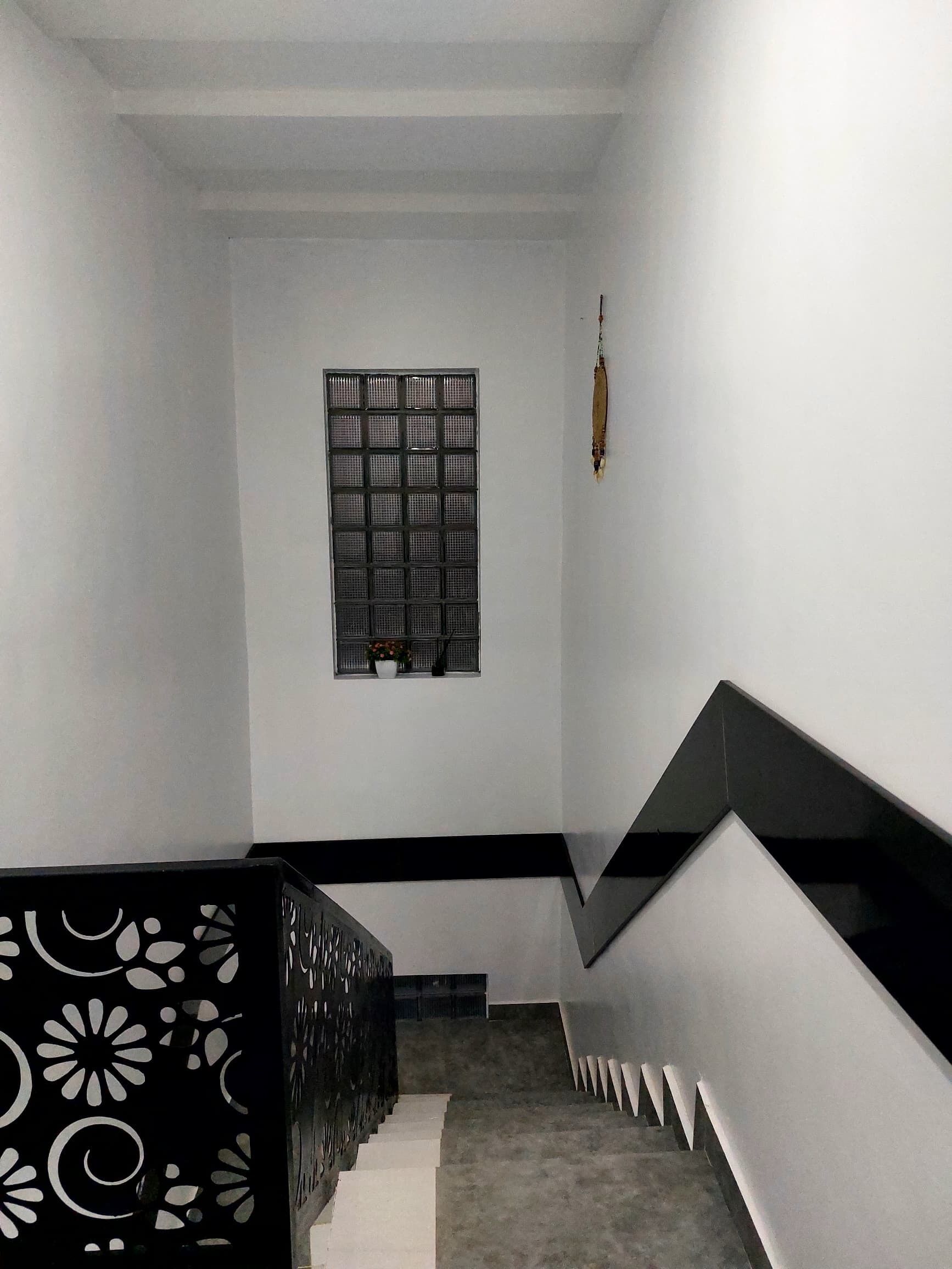 Una escalera con barandilla negra y paredes blancas que lleva a un rellano con una ventana y un adorno colgante.