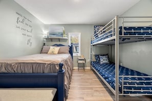 Une chambre avec un lit superposé, un lit simple et un mur décoré sur le thème de la marine.