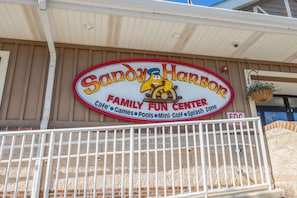 Une enseigne pour le Sandow Harbor Family Fun Center, avec un personnage de dessin animé et des installations telles qu’un café, des jeux, des piscines, un mini-golf et un espace de jeux aquatiques.