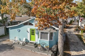 A small, single-story mobile home with a bright green door, a covered porch with chairs, and a small table. - Coastal Haven Getaway, Beach Stay & Resort Perks! (Myrtle Beach)