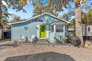 Une maison de plain-pied avec une porte d’un vert éclatant, une véranda couverte avec quatre chaises et un barbecue.