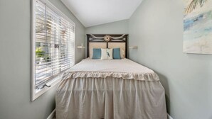 Quarto com cama, janela com persianas, luminária no teto e pintura pendurada na parede.