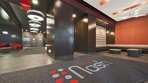 Un vestíbulo moderno con mostrador de recepción, zona de estar y alfombra estampada con el logotipo del hotel.