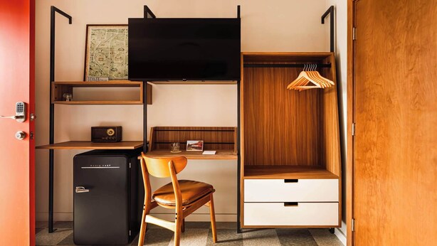Quarto compacto com escrivaninha, cadeira, guarda-roupa e um pequeno frigorífico.