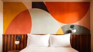 Quarto de hotel com cama, cabeceira de madeira e uma grande pintura abstrata na parede.