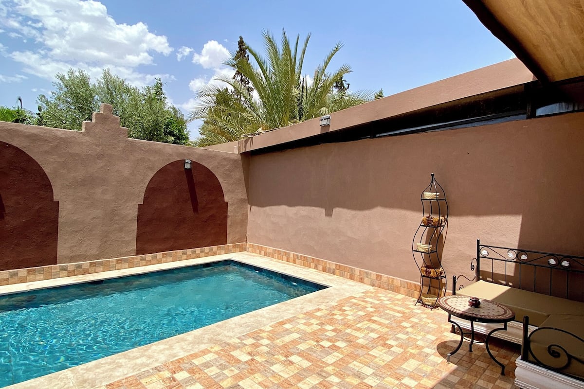 Une piscine dont le sol est recouvert de carreaux, avec un banc en métal et une étagère décorative en métal.