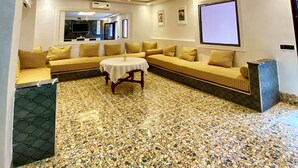 A spacious living room with a large sectional sofa, a round coffee table, and a television mounted on the wall. - Villa des roses privée (Marrakech)
