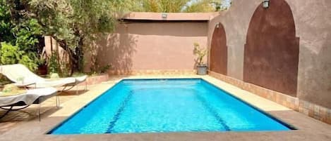 Una piscina con un borde de baldosas, rodeada por un muro bajo y palmeras.