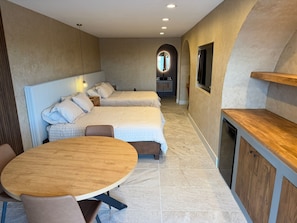 Ett modernt hotellrum med två sängar, ett matbord och ett litet kök.