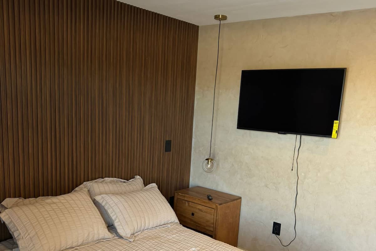 A bedroom with a bed, wooden headboard, bedside table, and a mounted TV.
