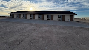 A motel with a row of rooms, a parking lot, and a dirt ground. - Presidio Inn (Presidio)