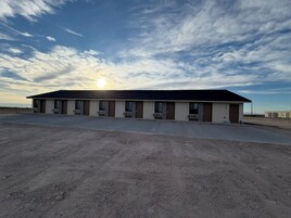 A motel with a row of rooms, a parking lot, and a dirt ground.