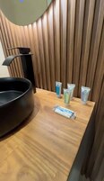 Un tocador de madera con un lavabo negro, tres tubos de artículos de tocador y un producto limpiador facial.