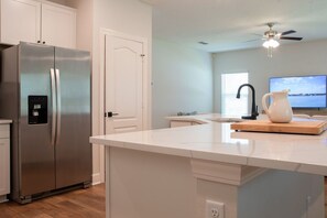 A modern kitchen with a stainless steel refrigerator, a white countertop, a ceiling fan, and a television. - St. Augustine 3BR | Near Downtown & Beaches (St. Augustine)