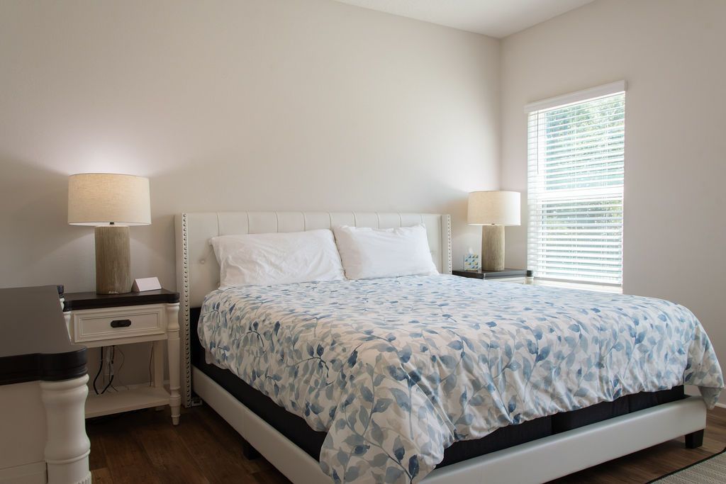 A bedroom with a bed, two bedside tables, and a window with blinds.