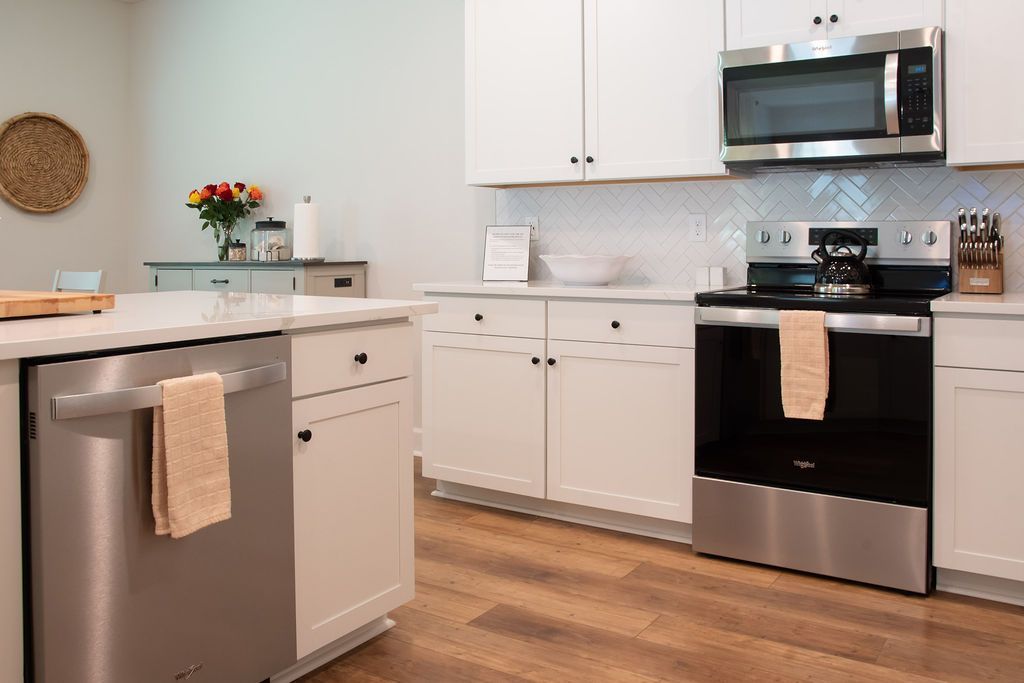 Une cuisine moderne avec des meubles blancs, des appareils en acier inoxydable et un dosseret de carrelage disposé en motif chevron.