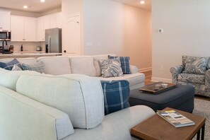 A modern living room with a sofa, ottoman, and armchair, a coffee table, and a kitchen in the background. - St. Augustine 3BR | Near Downtown & Beaches (St. Augustine)