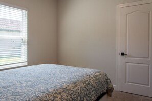 Ein Schlafzimmer mit einem Bett, einer Tür und einem Fenster mit Jalousien.