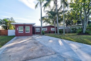 A single-story house with a red exterior, a front yard, and a driveway leading to the entrance. - Enjoy 3-Bedroom House with AC, Heated Pool and Gazebo in Charming Pinellas Park (Pinellas Park)