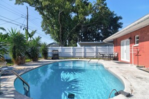 A swimming pool with a white fence, a barbecue grill, and a red building with a door. - Enjoy 3-Bedroom House with AC, Heated Pool and Gazebo in Charming Pinellas Park (Pinellas Park)