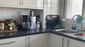 A kitchen with white cabinets, a black countertop, and a window. - Colorful 1 bedroom Flat in South East London area (Bromley)