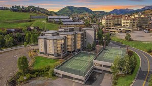 Un hotel de varios pisos con cancha de tenis, rodeado de vegetación y montañas.