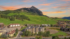 Un paisaje montañoso con un pico prominente, una zona residencial con edificios de varios pisos, y una carretera que conduce a ellos.