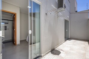 A modern residential space with a glass door leading to a bathroom, a tiled patio, and a white exterior wall. - Apt w/ Barbecue Grill 190 m From the Beach Mbu0102 (Barra Velha)