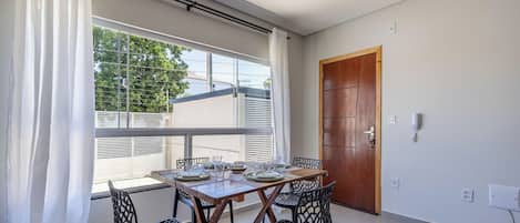 A dining area with a table set for four, a wooden door, and a window with curtains.