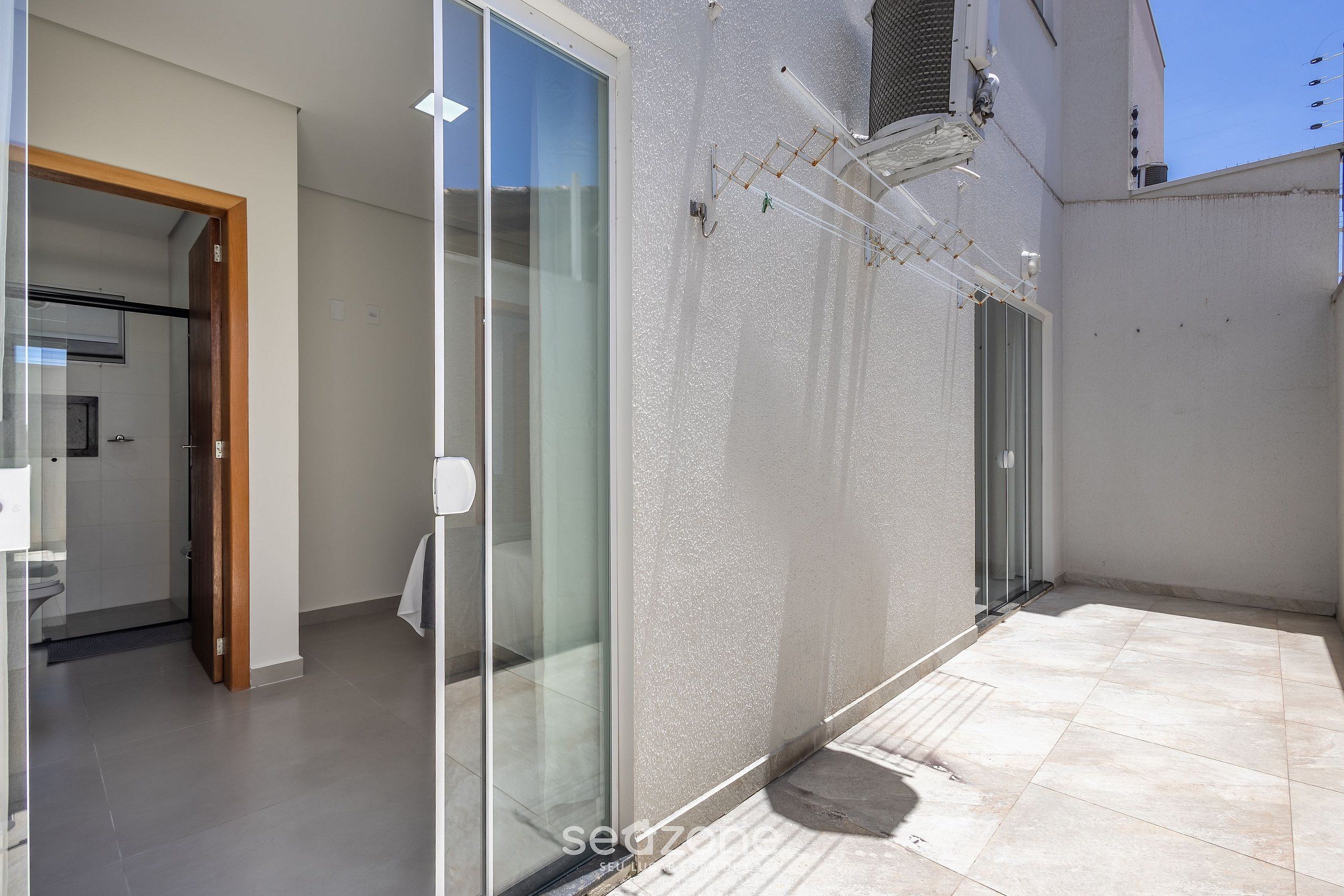 A modern residential space with a glass door leading to a bathroom, a tiled patio, and a white exterior wall.