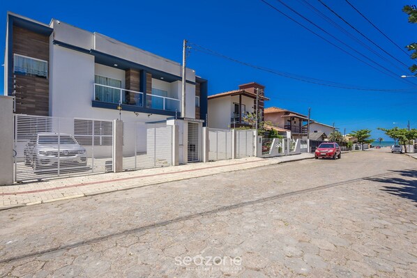 A modern two-story house with a gated driveway and a red car parked on the street. - Apt w/ Barbecue Grill 190 m From the Beach Mbu0102 (Barra Velha)