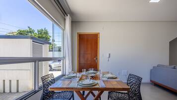 A dining area with a wooden table set for four, surrounded by black chairs, a grey sofa, and a wooden door.