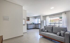 Een moderne woonkamer met een grijze bank, een eethoek met een tafel en stoelen, en een keuken op de achtergrond.