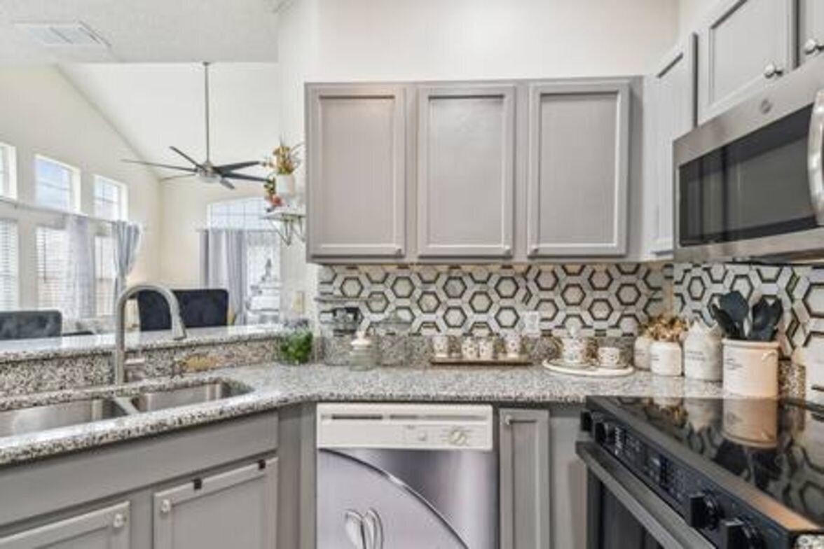 A modern kitchen with grey cabinets, a stainless steel dishwasher, a microwave, and a granite countertop.