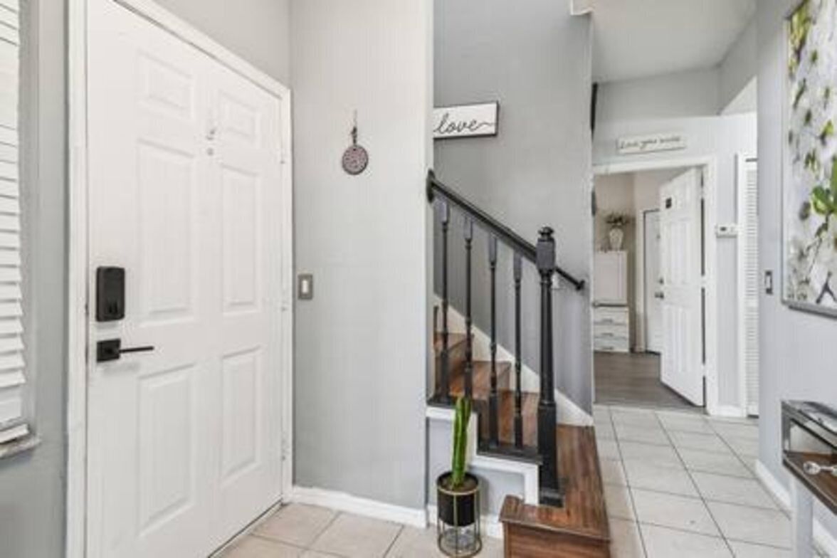 A hallway with a white door, a potted plant, and a staircase with a black railing.