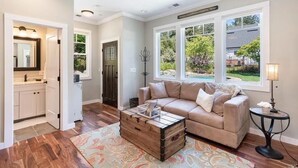 A spacious living room with a beige sofa, a wooden coffee table, and a view of a backyard through large windows.