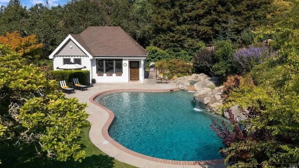A house with a swimming pool surrounded by lush greenery and a small waterfall feature.
