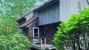 A rustic wooden house with a stone foundation, a wooden porch, and a stone pathway leading to the entrance. - Waterville Estate chalet perfect for relaxing stays Access to Pool, Hot Tub, Gym (Campton)