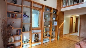 A spacious living area with wooden shelving filled with books and decorative items, a large clock on the wall, and a view of the upper floor. - Waterville Estate chalet perfect for relaxing stays Access to Pool, Hot Tub, Gym (Campton)