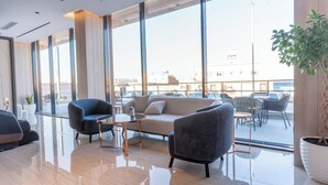 Un área de estar moderna con sofá, sillones y una mesa de centro. Amplias ventanas ofrecen vistas panorámicas de la ciudad.