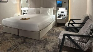 Una habitación de hotel moderna con una cama grande, un sofá, un televisor y una mesita de noche con lámpara.