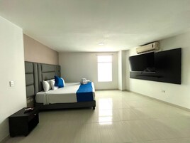 Una habitación de hotel con cama, televisor montado en la pared, ventana y suelo de baldosas.