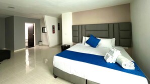 Une chambre d’hôtel avec un lit, une table de chevet, une tête de lit et une salle de bain visible à travers une porte ouverte.