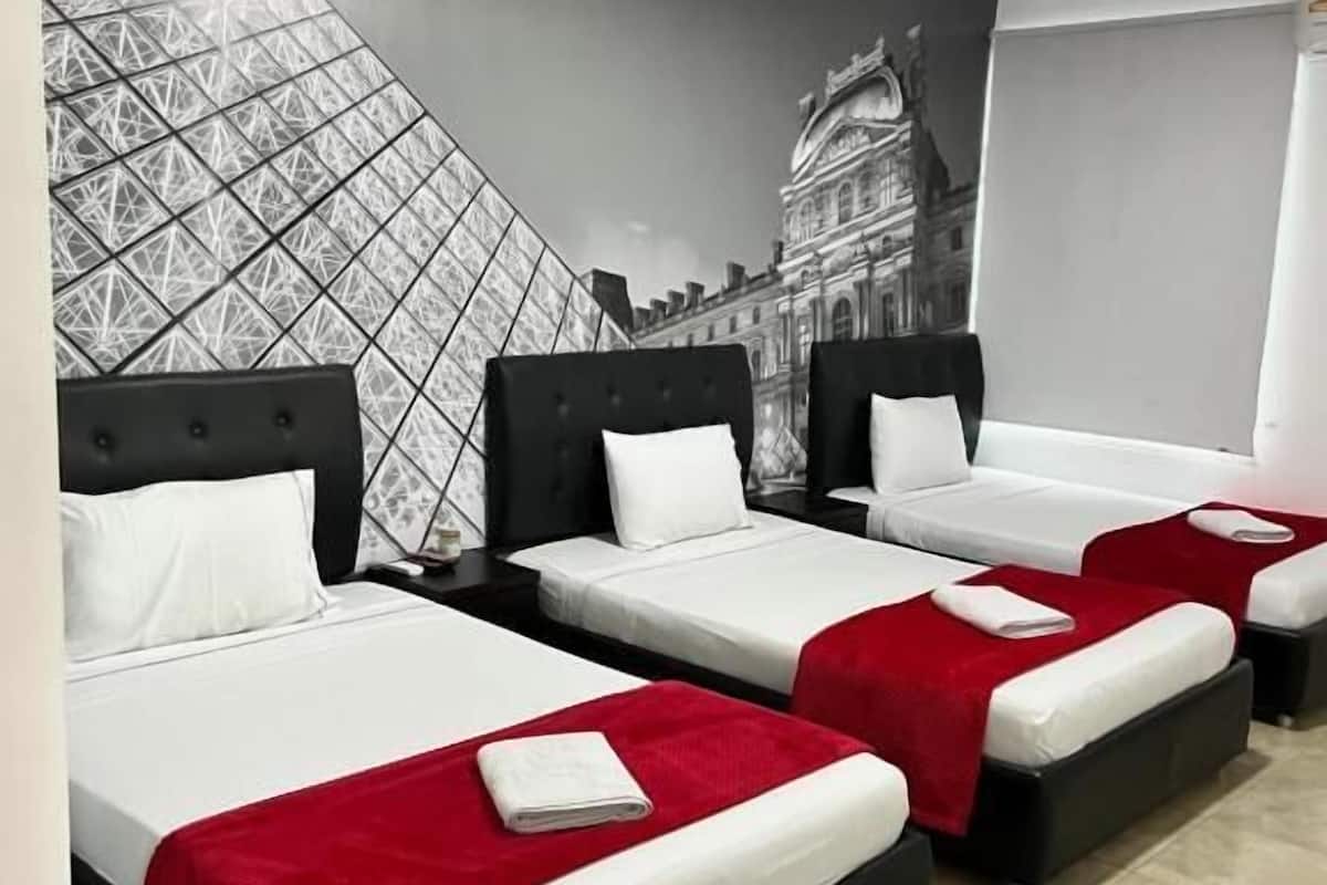 Ein Hotelzimmer mit drei Betten, jedes mit einem schwarzen Kopfteil und weißer Bettwäsche. Ein großes Wandbild zeigt eine Stadtansicht.