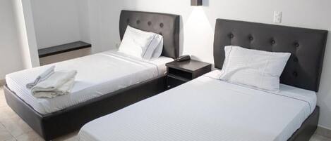 Zwei Betten mit je einem Einzelbett, ein Nachttisch mit Lampe und ein hängender Duschvorhang.