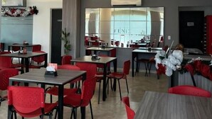 Un espace repas moderne avec des chaises et des tables rouges, une cuisine en arrière-plan et une vue sur la ville à travers de grandes fenêtres.