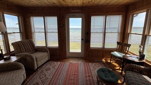 Una baita dall'interno in legno, con ampie finestre, un tappeto decorato e vista sull'acqua.