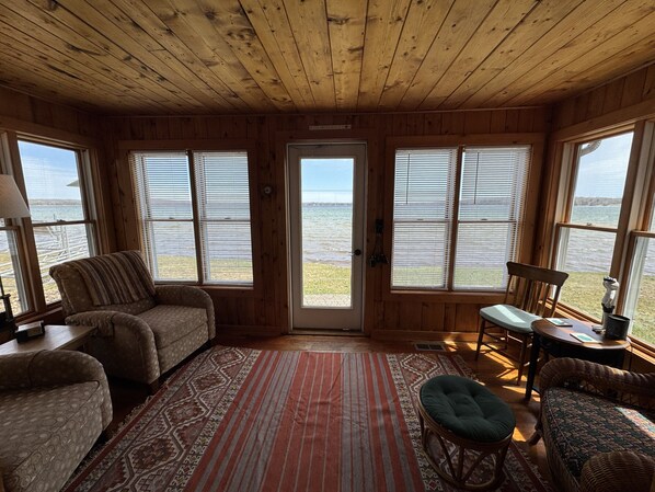 A cabin with a wooden interior, large windows, a patterned rug, and a view of the water.